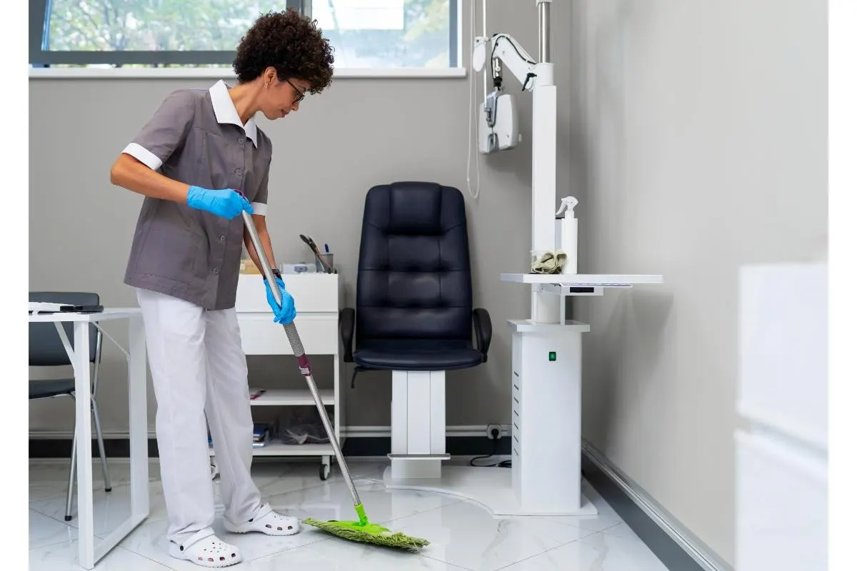 Cleaner in uniform and gloves mopping the floor of a medical examination room in London