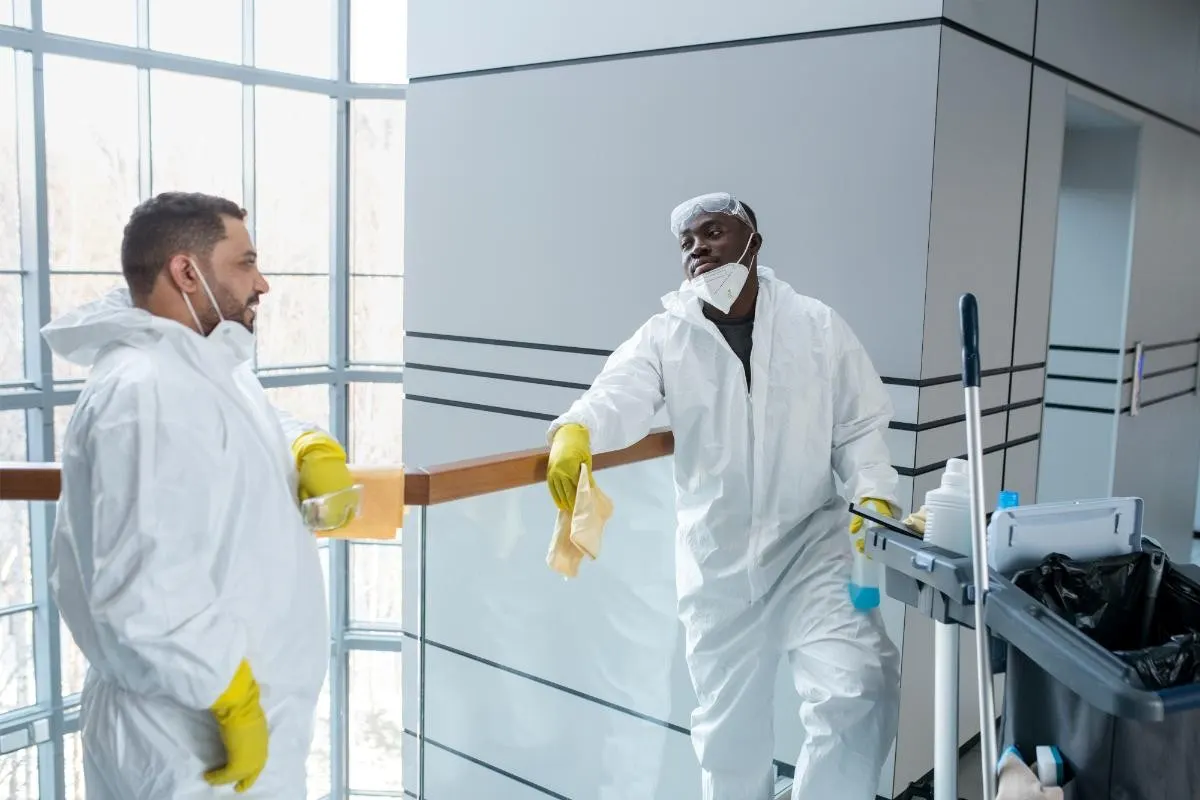 Two cleaners in protective suits and masks discussing work in a modern London office building