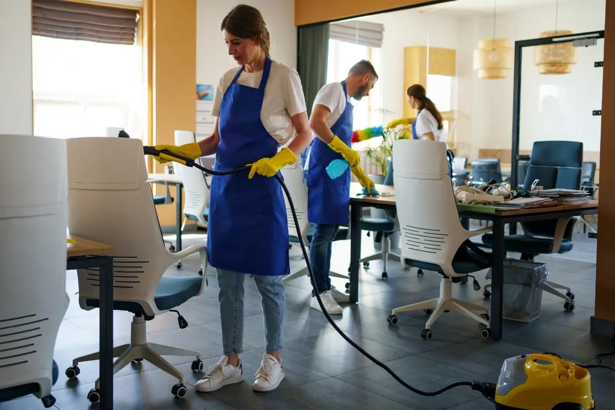 Professional cleaning team in blue aprons steam cleaning and sanitising a London office space